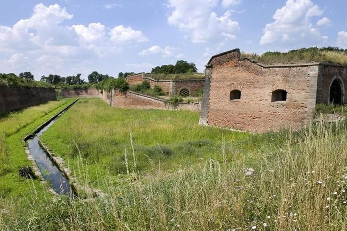 ein altes Backsteingebäude in einem Feld mit einem Graben