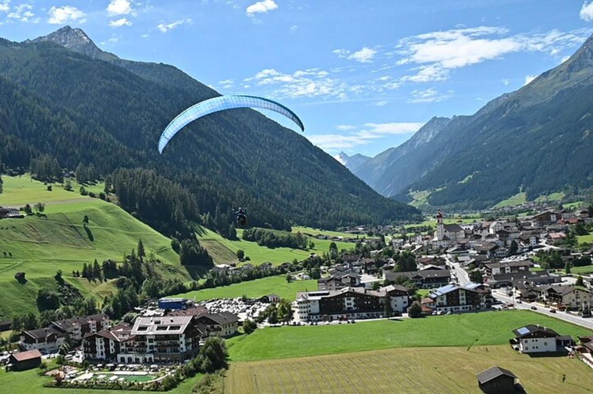 a paraglider flying over a village in the mountains
