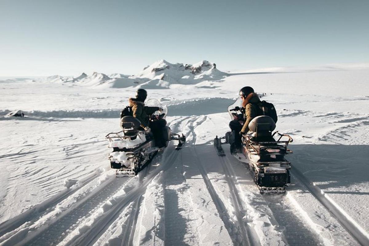 Tres personas viajando en vehículos todo terreno en la nieve