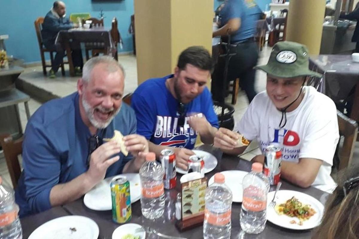 un gruppo di tre uomini seduti a un tavolo che mangiano cibo