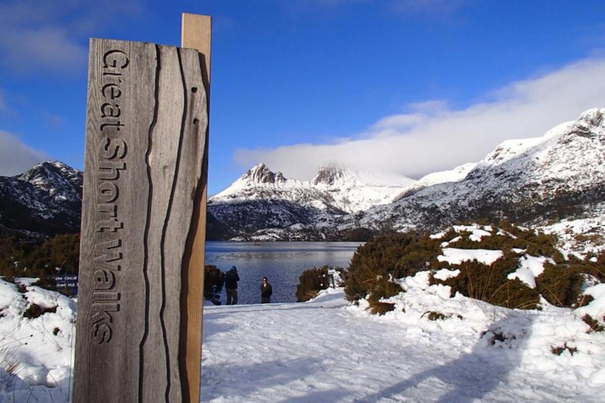 a wooden sign in the snow with mountains in the background