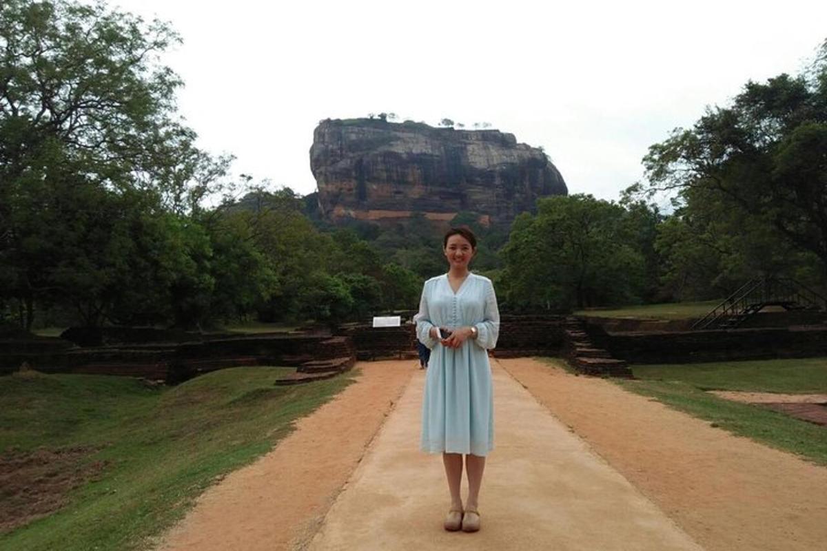 seorang wanita berdiri di atas jalan tanah dengan latar belakang gunung