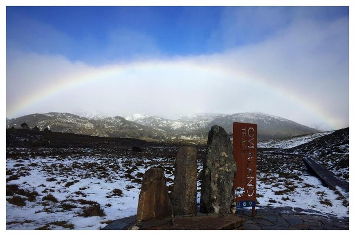 a rainbow over a snow covered field with a sign
