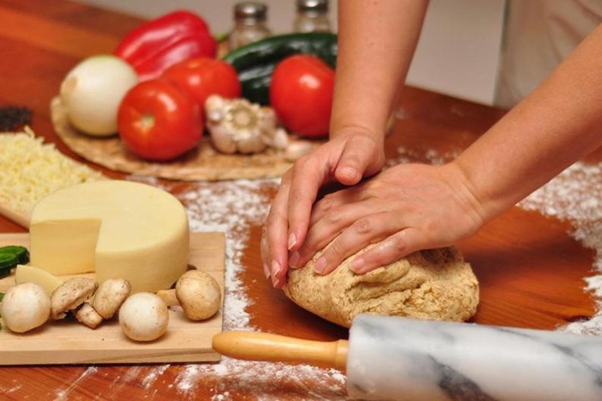 henkilö leipoo leipää pöydällä vihannesten kanssa