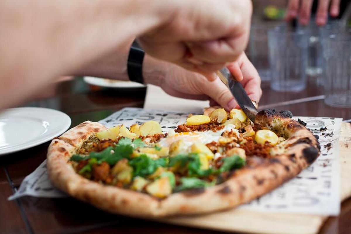 una persona cortando una pizza con cuchillo y tenedor