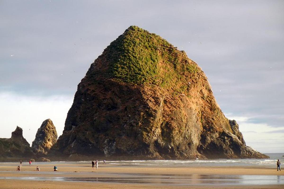 people standing on a beach near a large rock formation