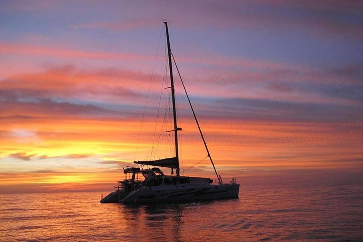 a sail boat sitting in the ocean at sunset