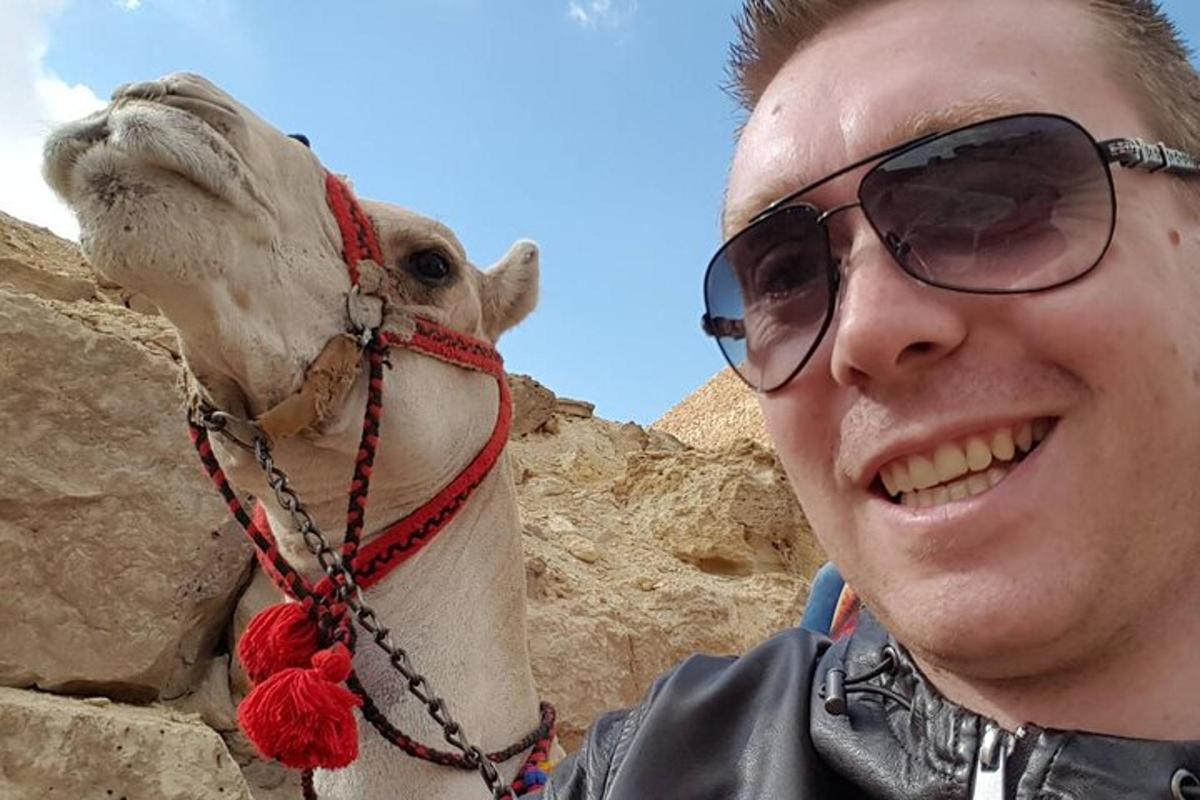 muž se slunečními brýlemi stojící vedle velblouda