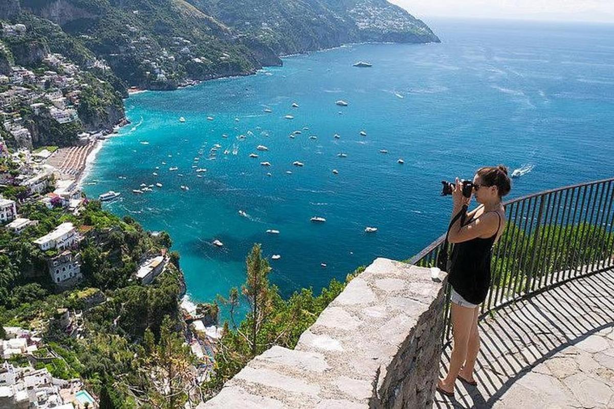 eine Frau, die auf einer Mauer steht und ein Foto vom Meer macht