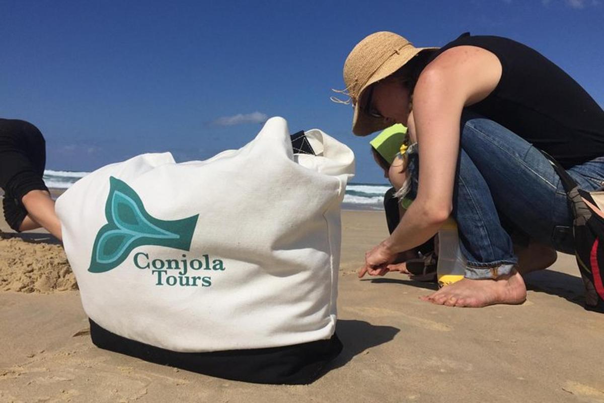 a woman sitting on the beach next to a bag