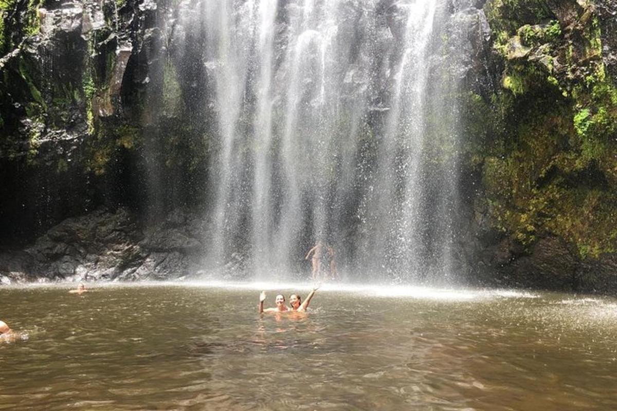 orang berenang di dalam air di hadapan air terjun