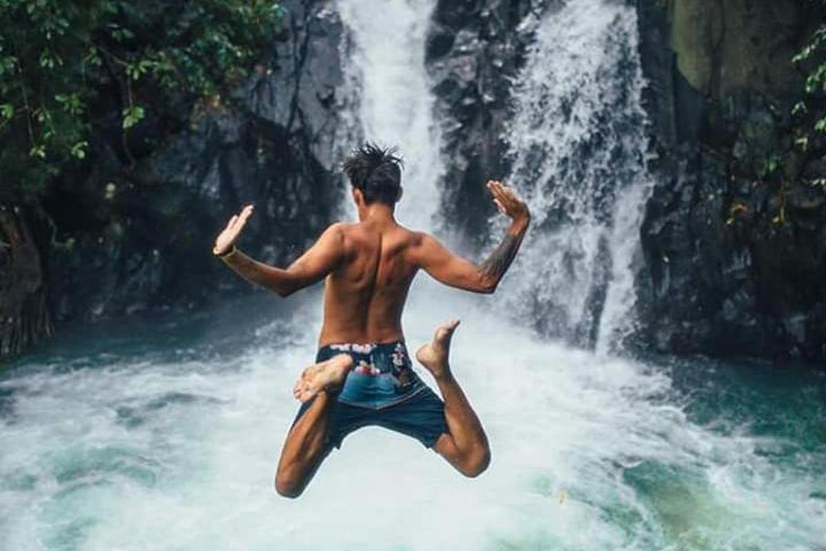 seorang lelaki melompat ke dalam air di hadapan air terjun