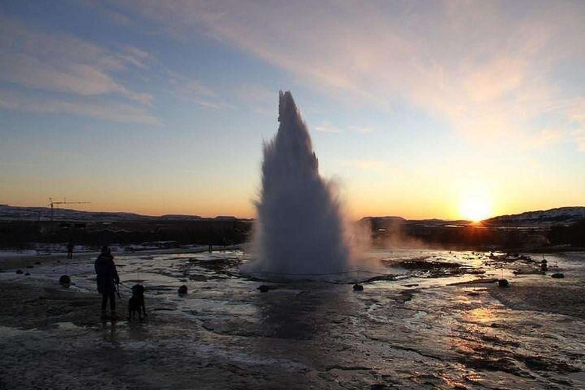 uma fonte de água em um campo com o pôr do sol
