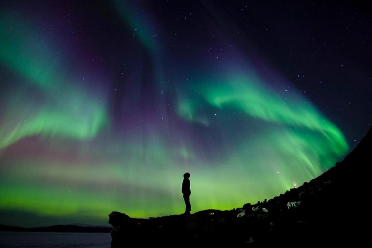 Un hombre parado sobre una roca bajo la aurora boreal.