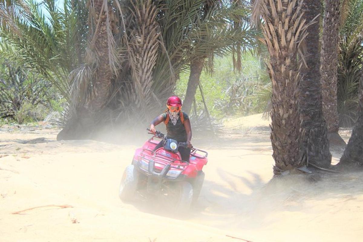 uma pessoa pilotando um quadriciclo vermelho na areia