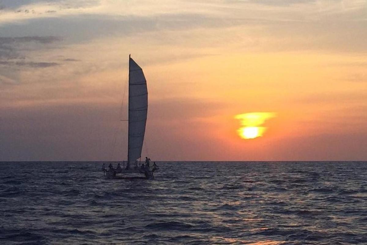 a sailboat in the ocean with the sunset in the background