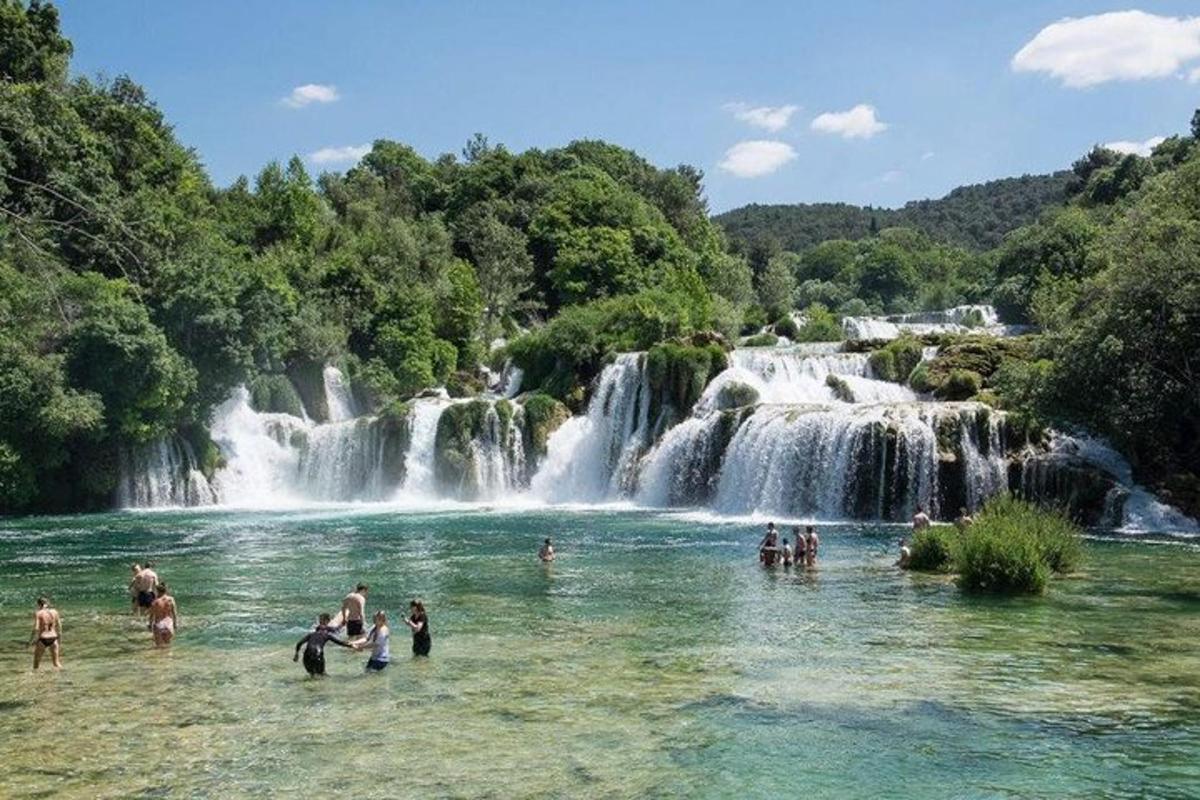 orang berenang di dalam air di hadapan air terjun