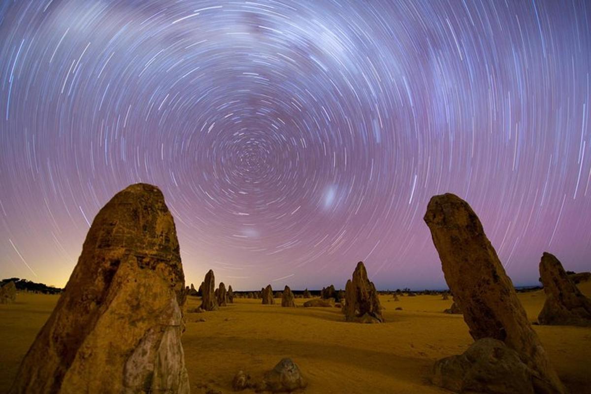 a star trails in the sky with rocks in the desert