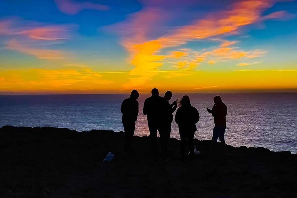 a group of people standing on top of a cliff watching the sunset