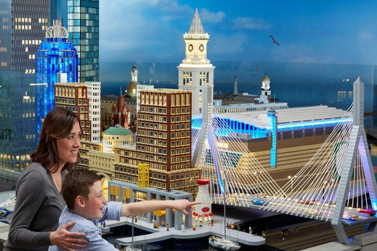 a woman and child playing with a lego model of a bridge