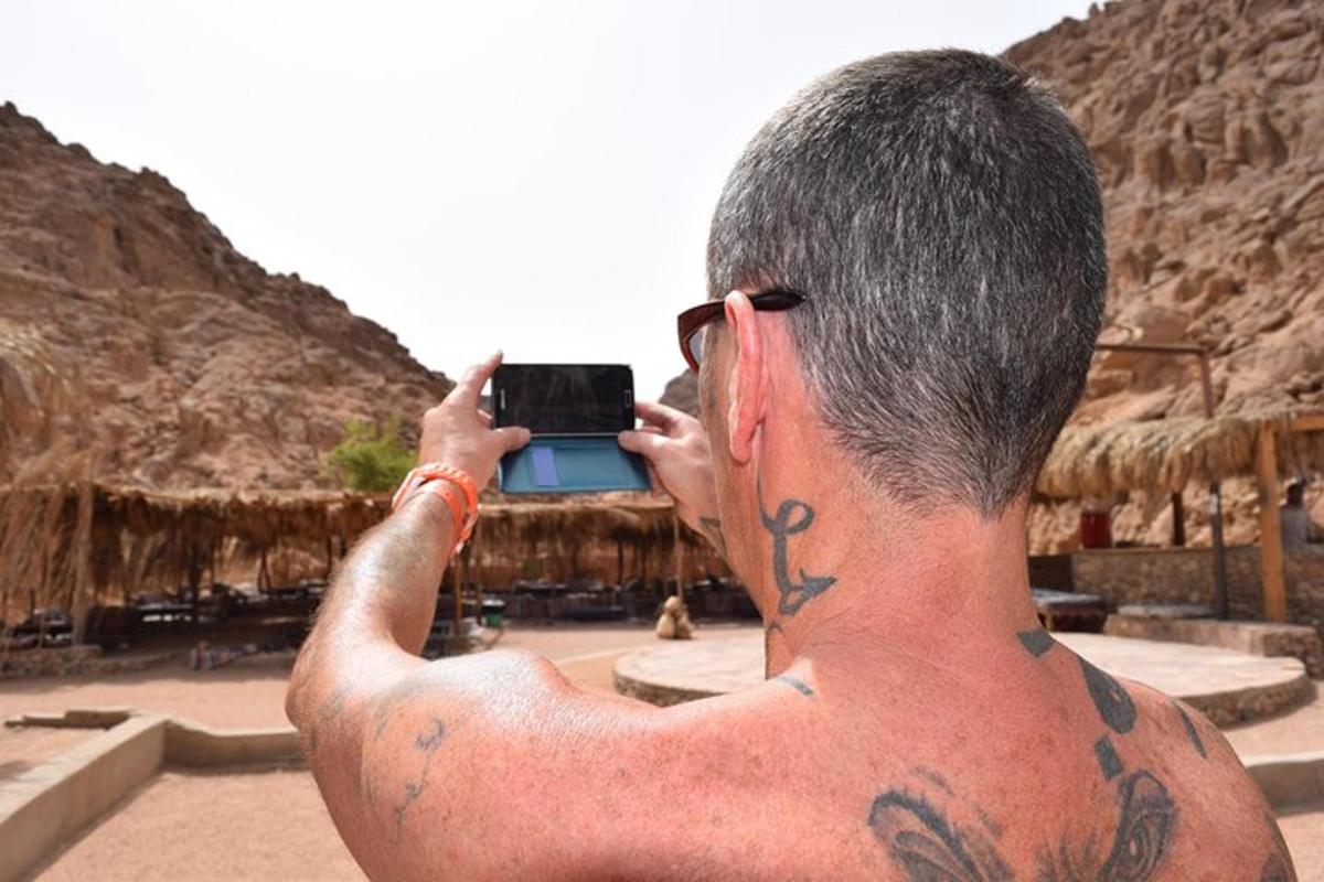 moški s tetovažami fotografira s svojim mobilnim telefonom