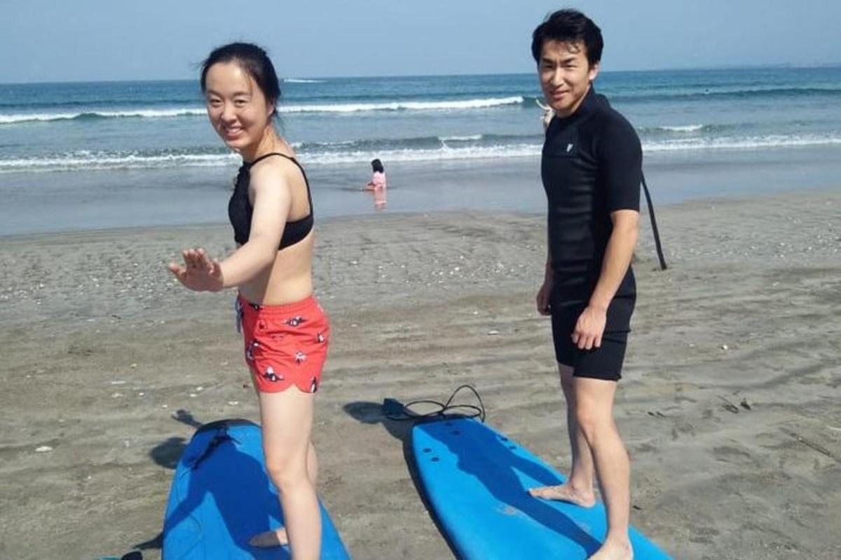 um homem e uma mulher em pé na praia com uma prancha de surfe