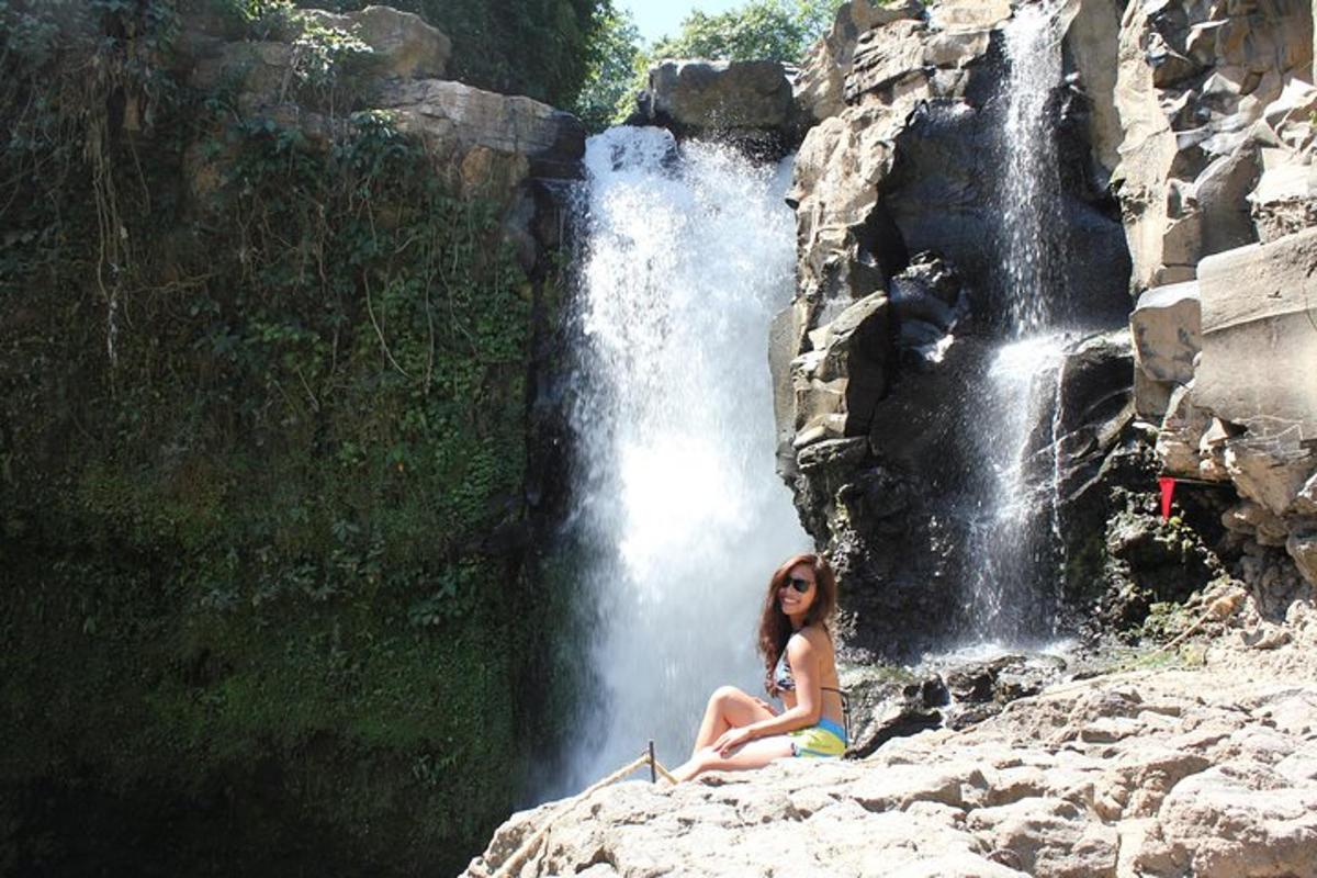a woman sitting on a rock in front of a waterfall
