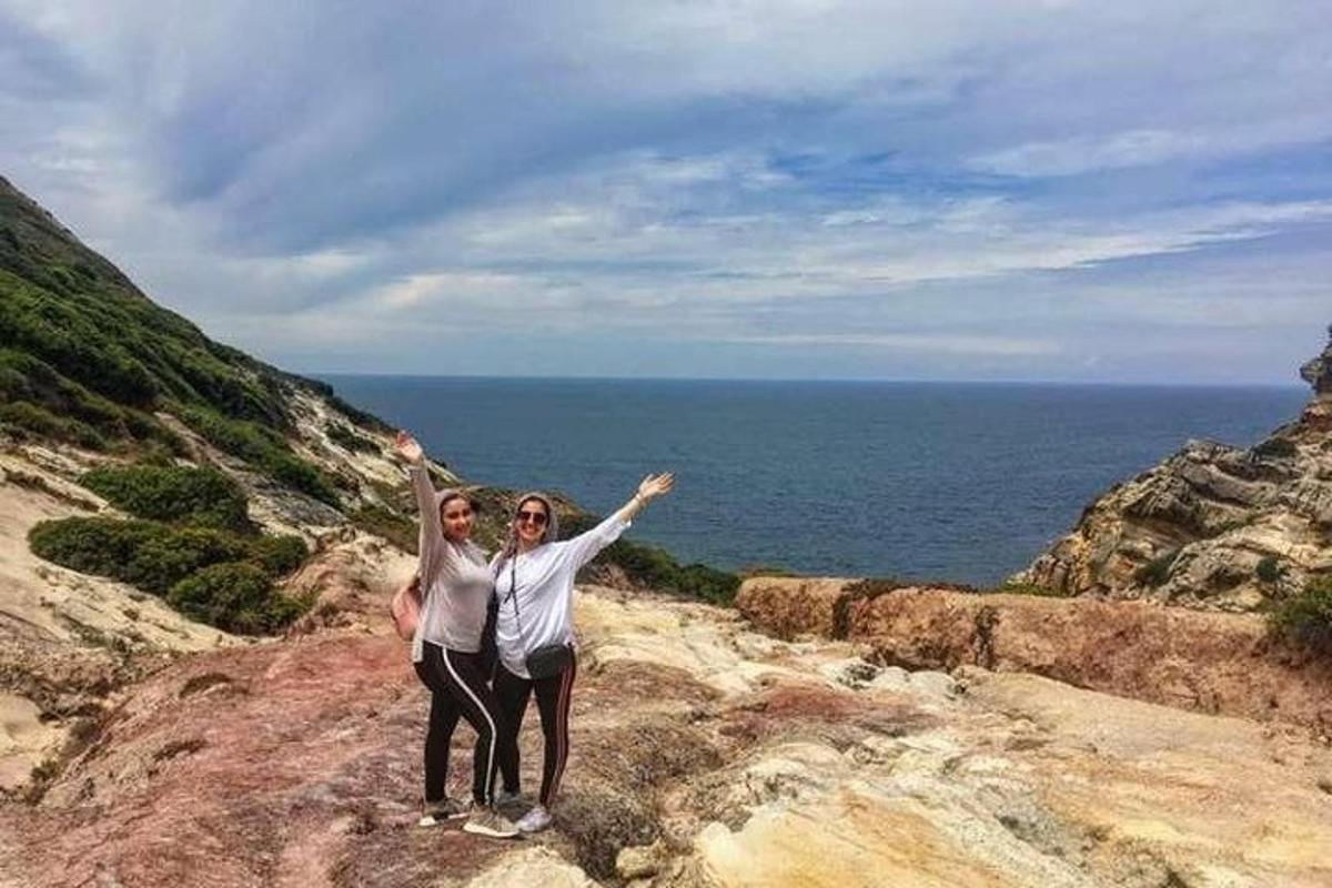 Dos personas de pie sobre una roca cerca del océano.