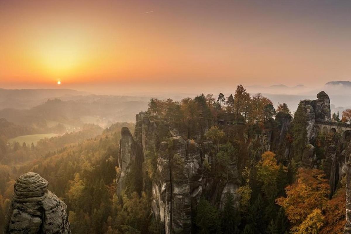 auringonlasku vuoren yllä puiden ja kivien keskellä