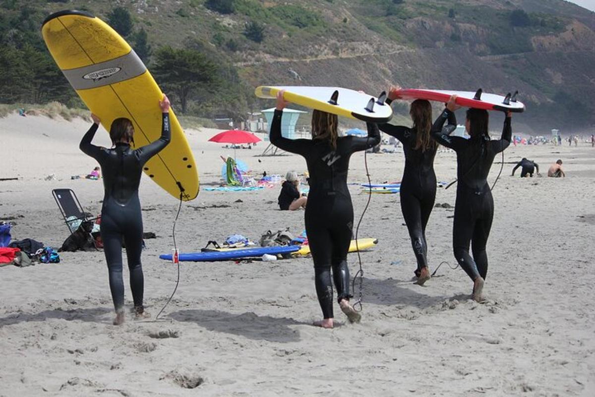 tre donne in muta che trasportano tavole da surf su una spiaggia