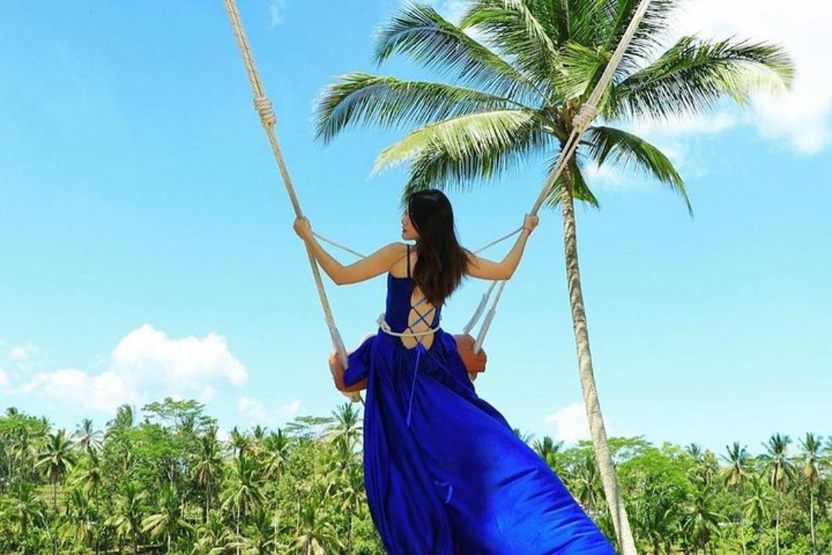 a woman in a blue dress swinging on a palm tree