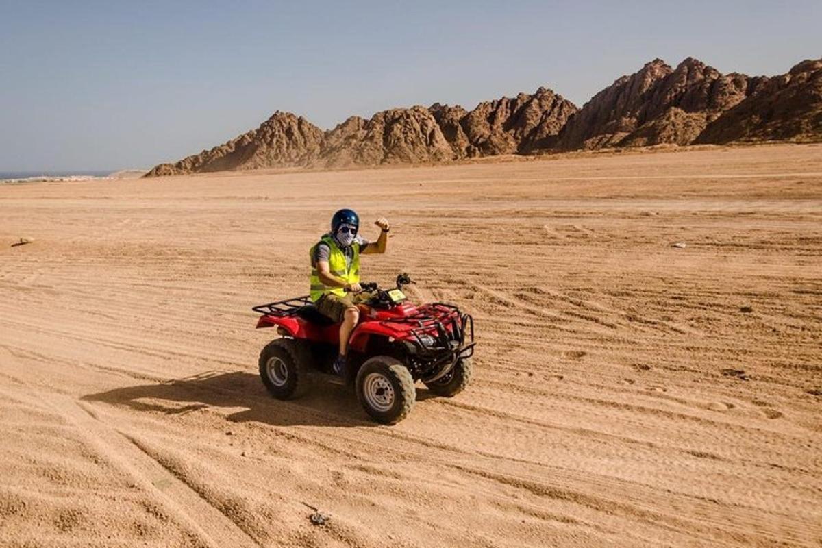 seseorang yang menunggang basikal quad di padang pasir