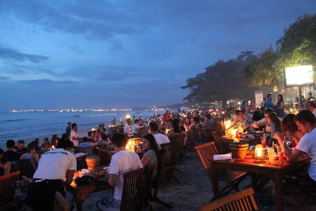 una folla di persone sedute ai tavoli sulla spiaggia di notte