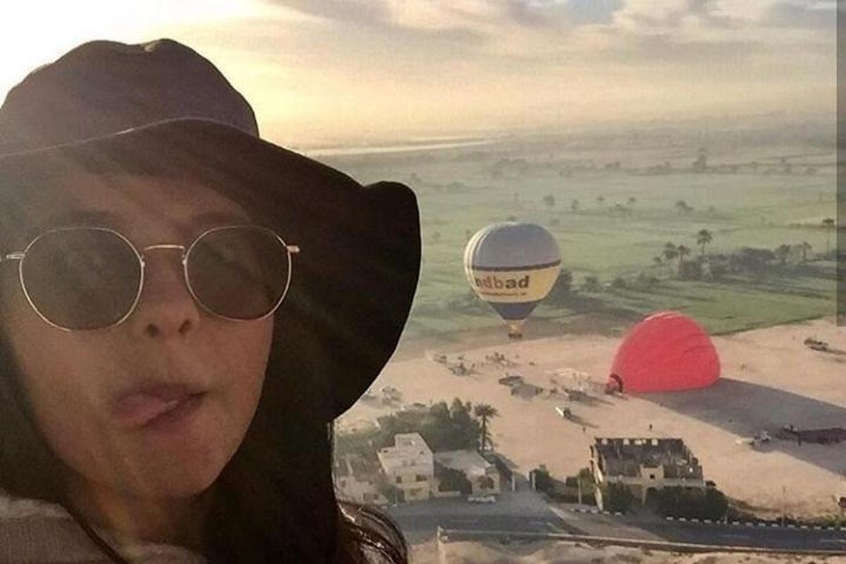 a woman wearing sunglasses and a hat looking at hot air balloons