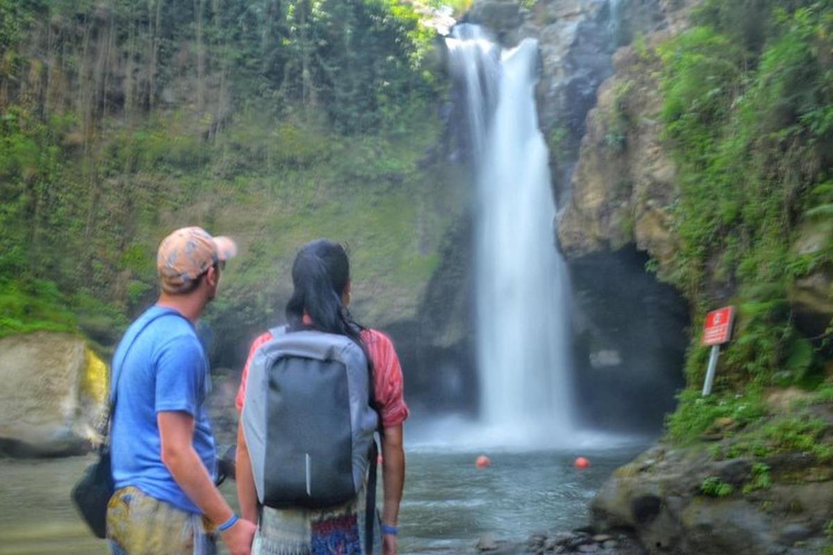 dua orang berdiri di hadapan air terjun
