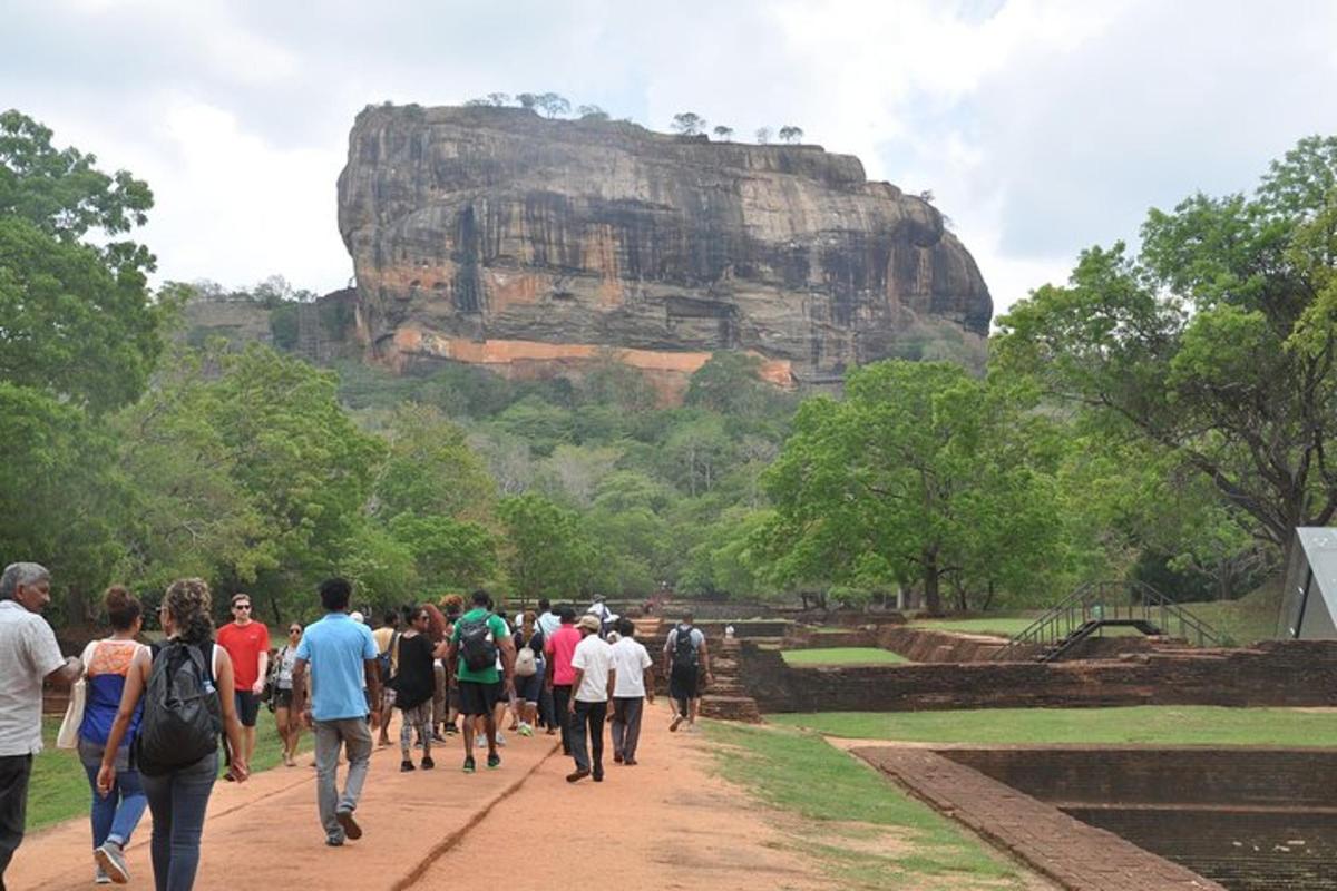 a group of people walking down a dirt road in front of a mountain