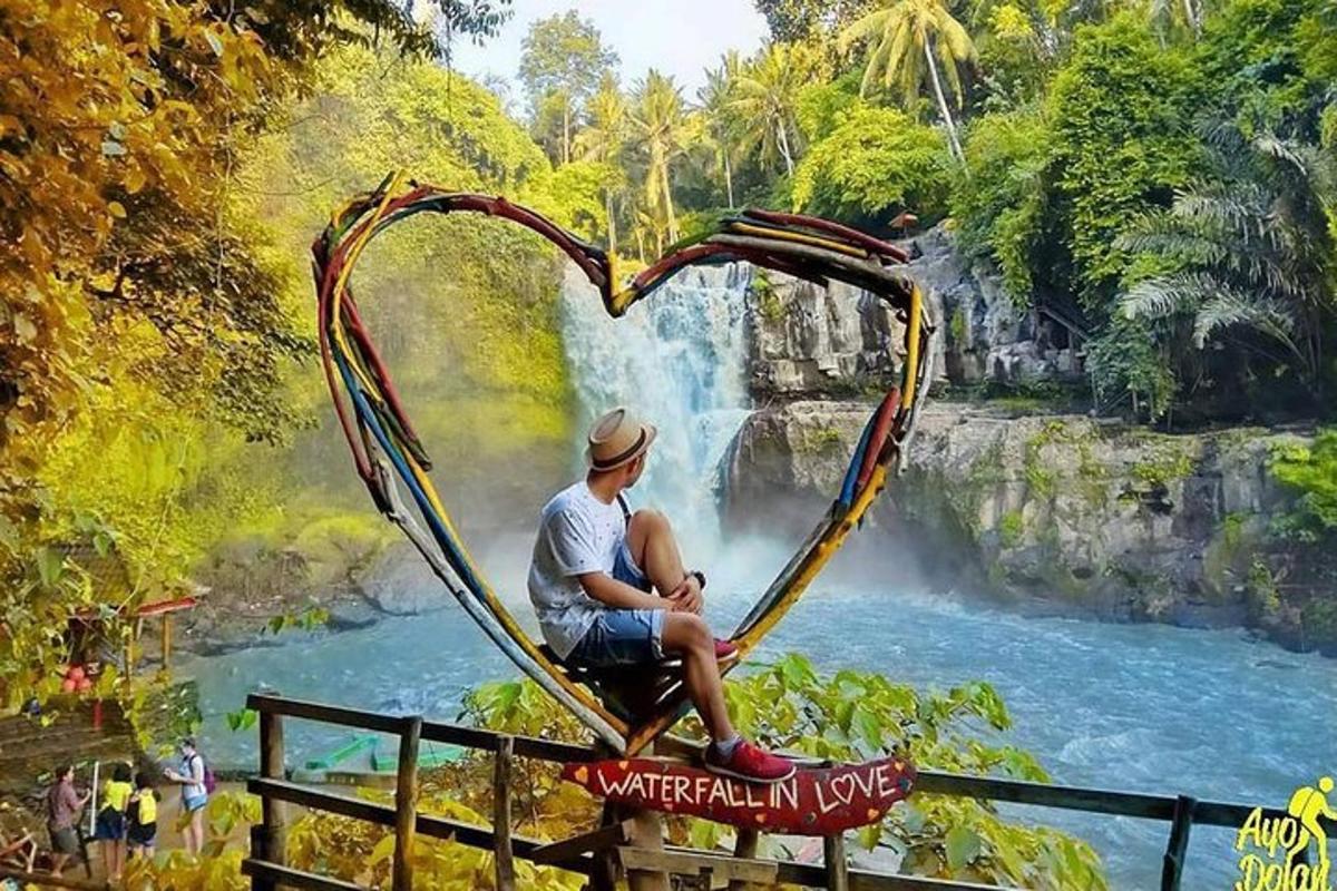 seorang pria duduk di tanda berbentuk hati di depan air terjun