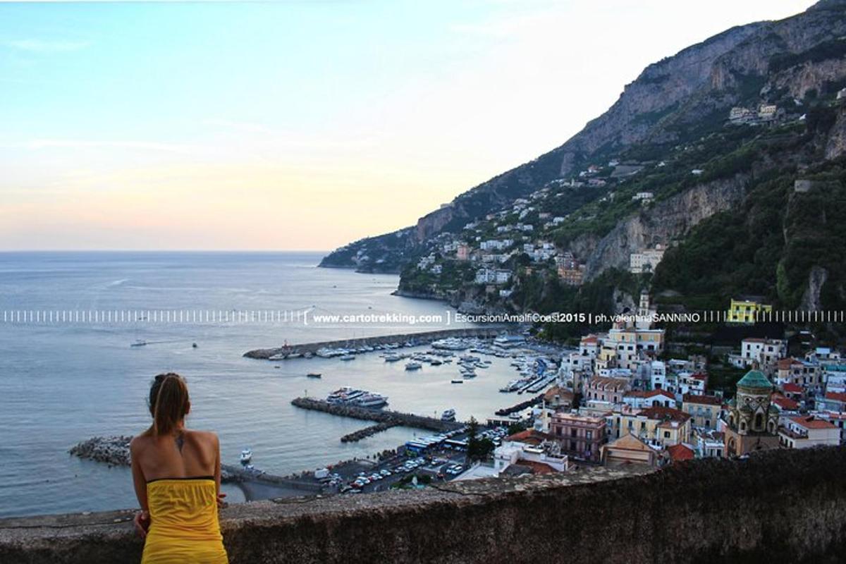 a woman in a yellow dress sitting on a wall looking at the ocean
