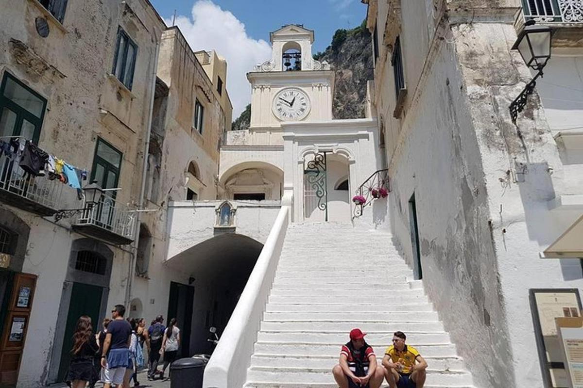 two people sitting on stairs in an alley with a clock tower