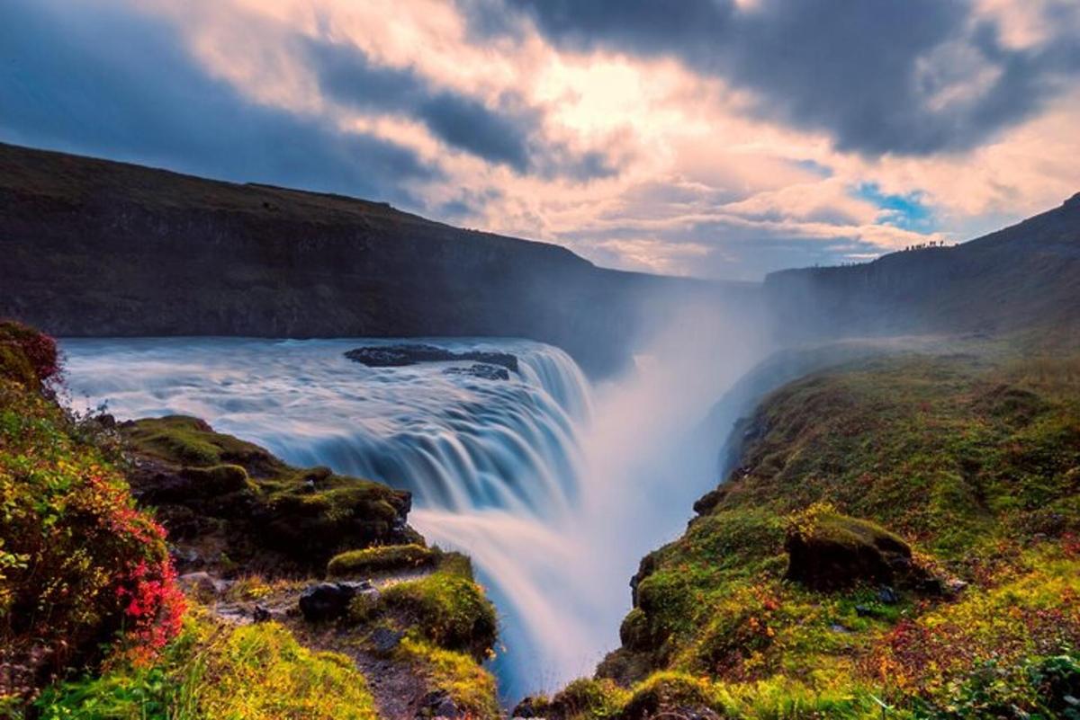 una cascada en la orilla de un río con un cielo nublado