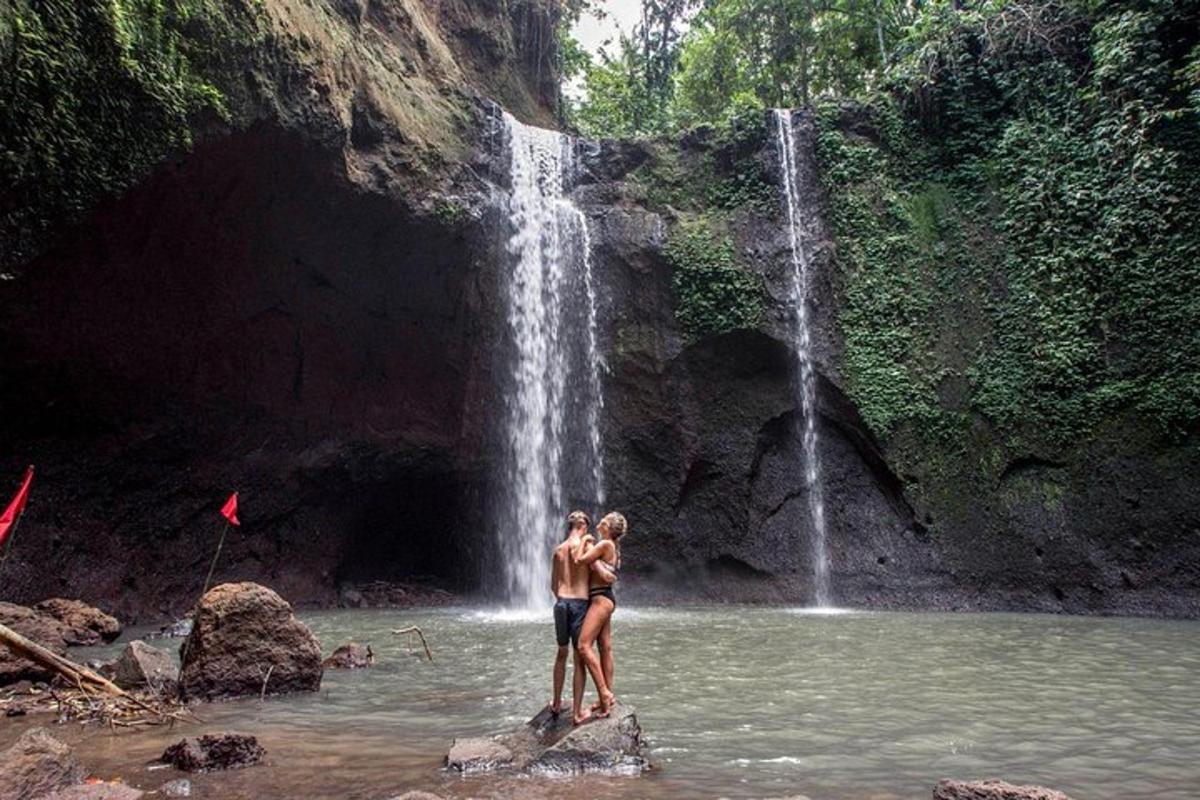 duas pessoas em pé na água em frente a uma cachoeira