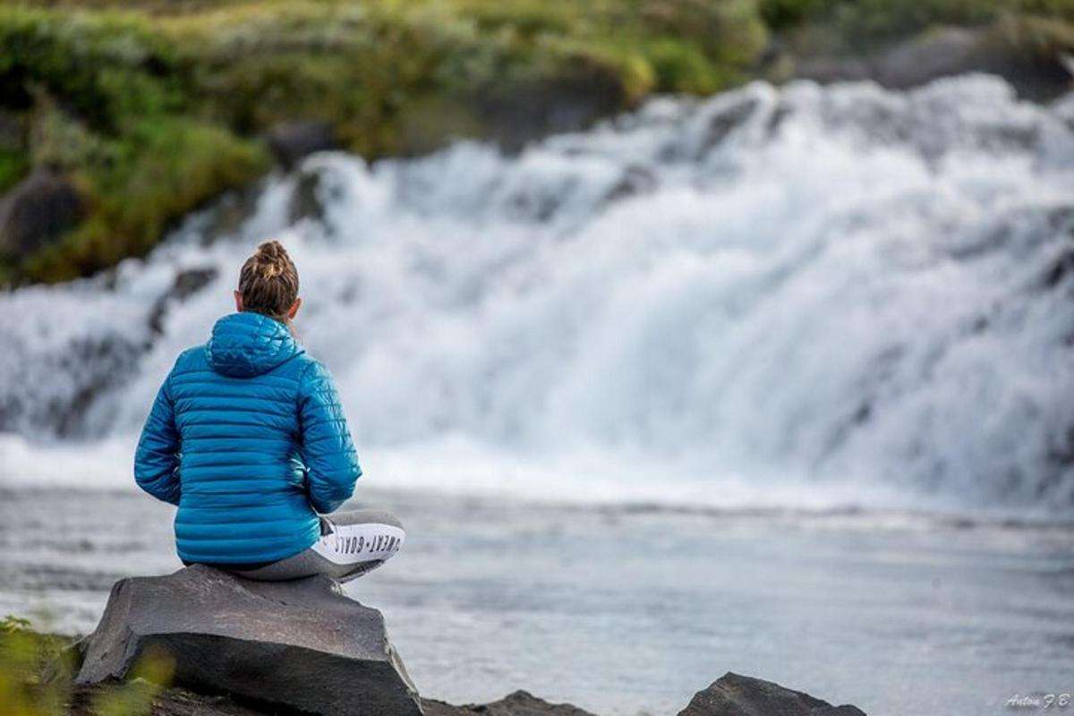 maður situr á steini og horfir á foss