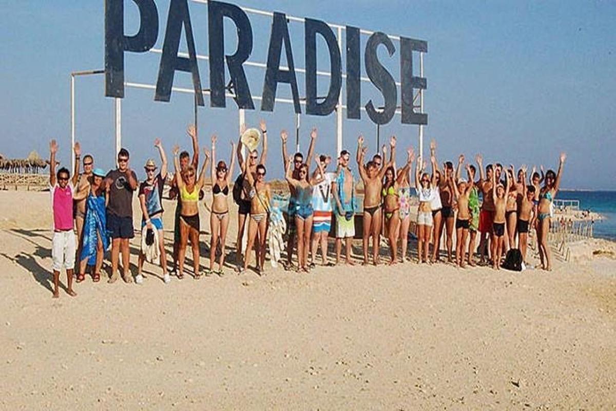 Un grupo de personas de pie en la playa sosteniendo un cartel grande.