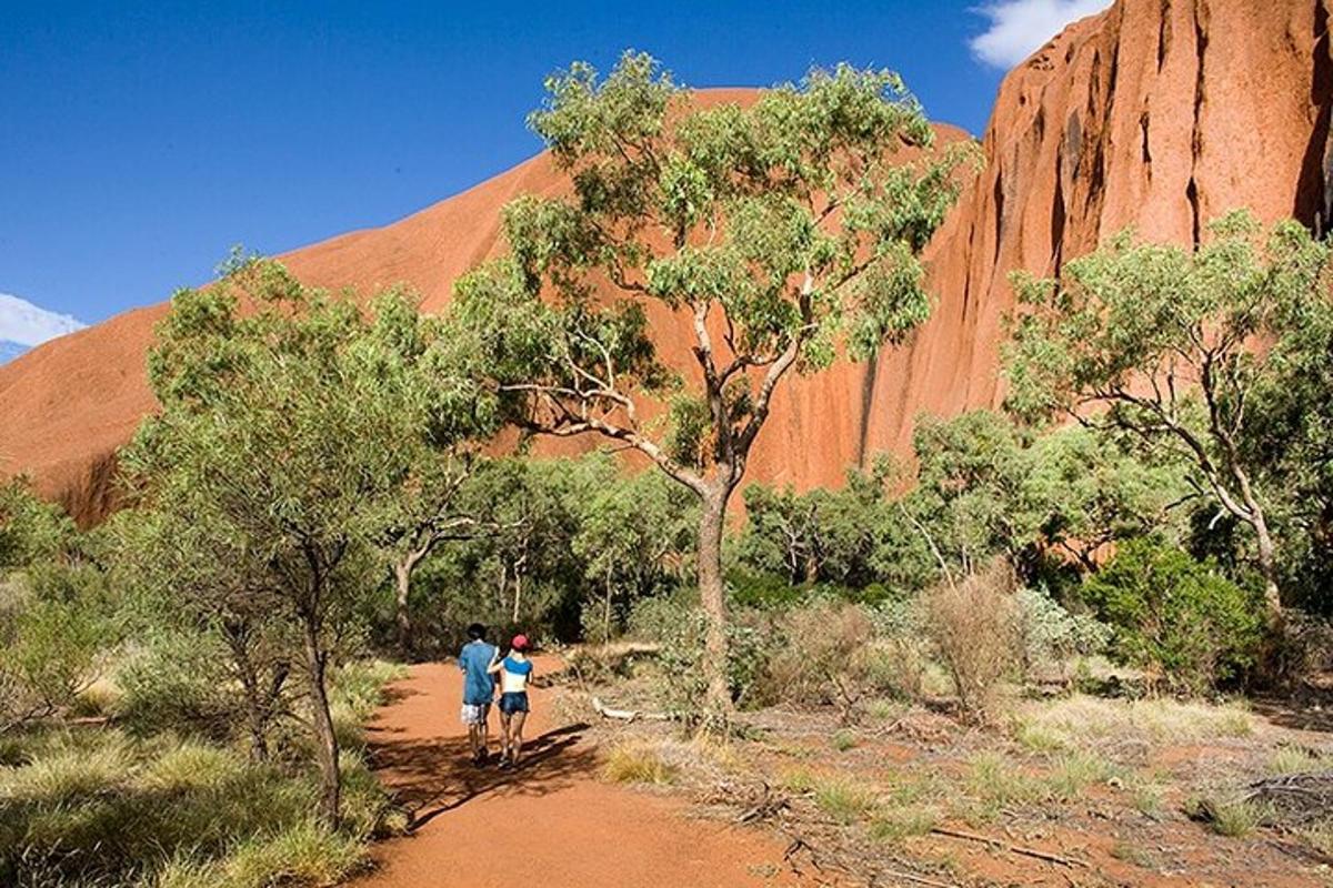 two people walking down a dirt road in front of ayers rock