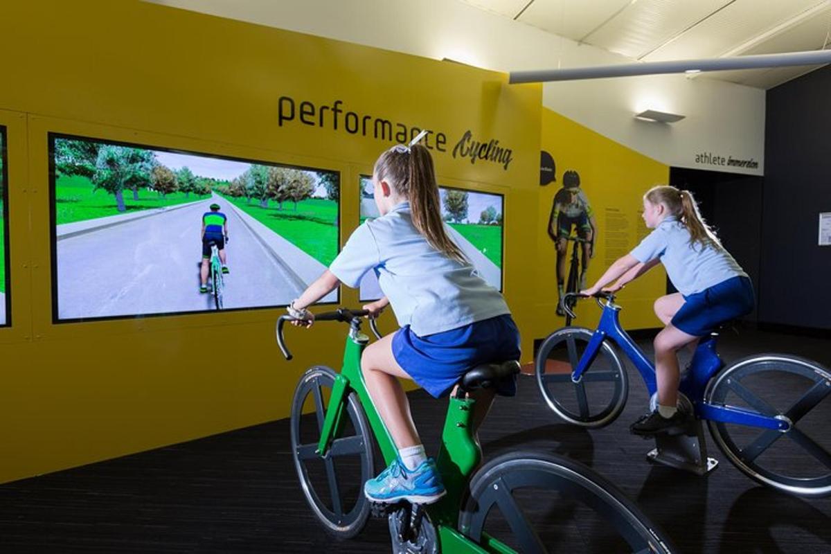 two girls riding bikes in a room with a video screen