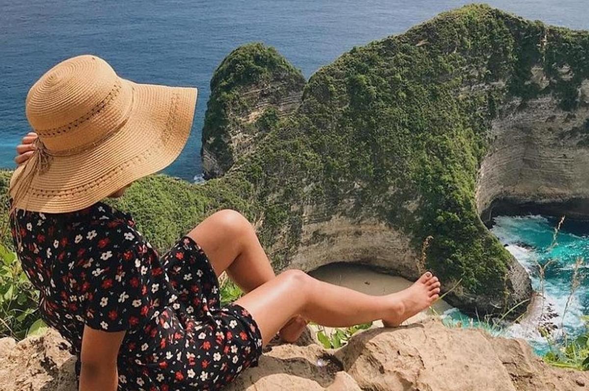 una donna con un cappello seduta su una roccia vicino all'oceano