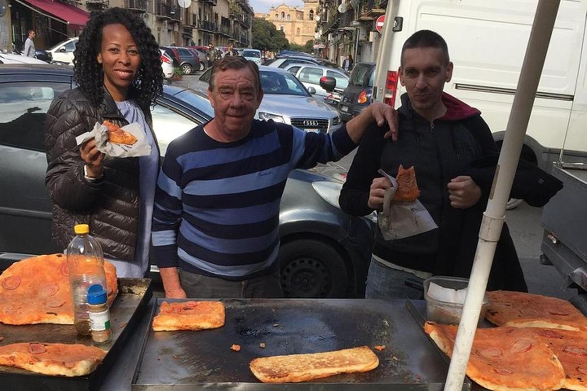 un home i dues dones drets al costat d'una graella amb pizza