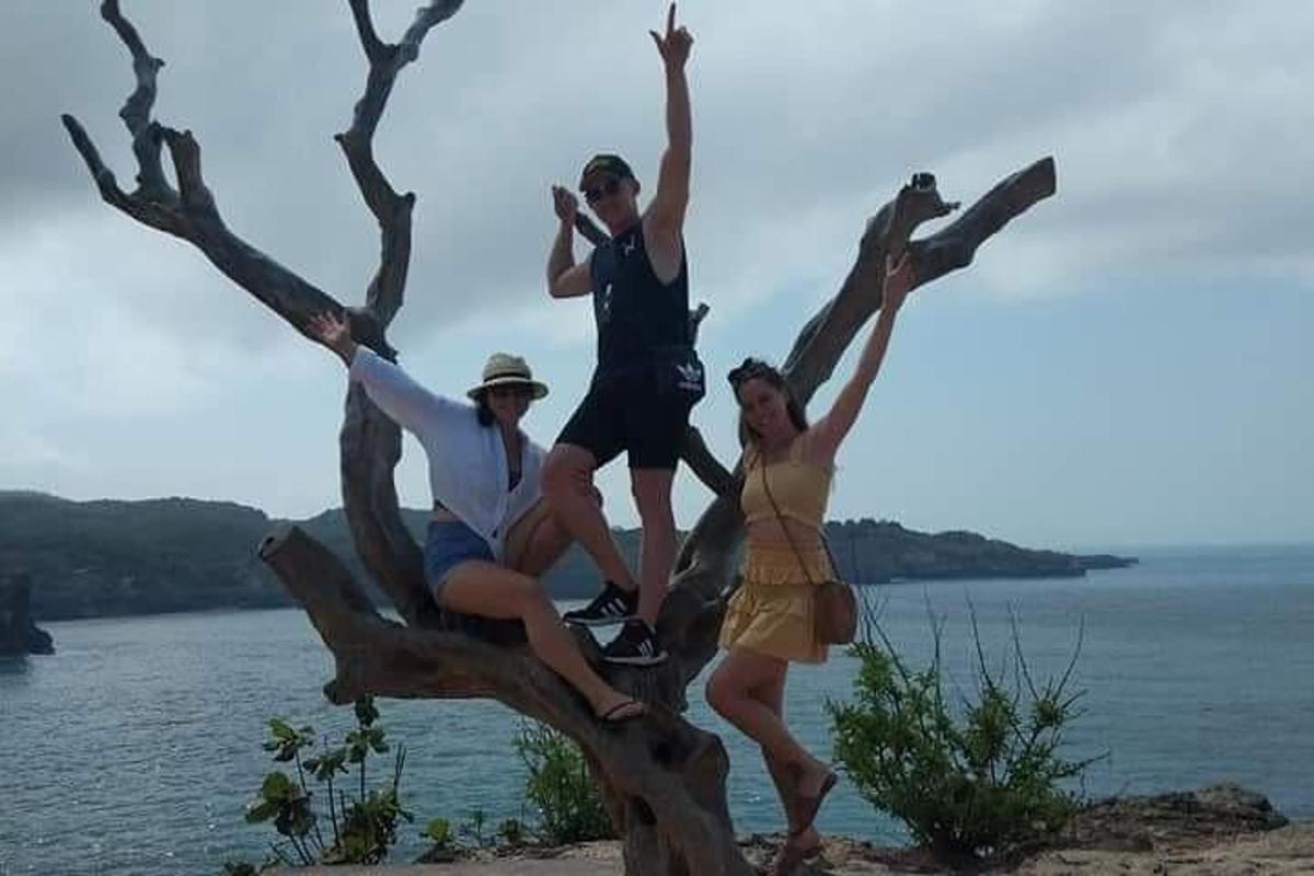 three people sitting on a tree branch near the water