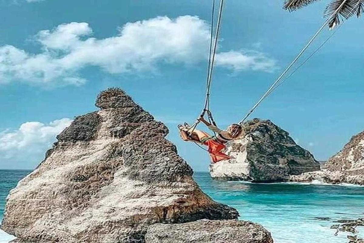 a person on a swing on a rock in the ocean