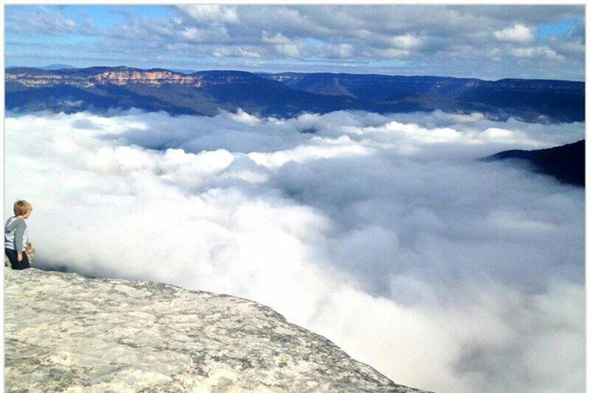 eine Person, die auf einem Berggipfel über den Wolken steht